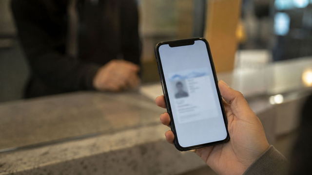 A driver holds up a smartphone displaying a mobile driver's license at a service counter